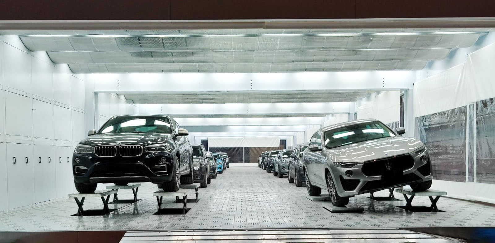 A long Saicozero spray booth with SUVs on paint platforms under bright LED lighting